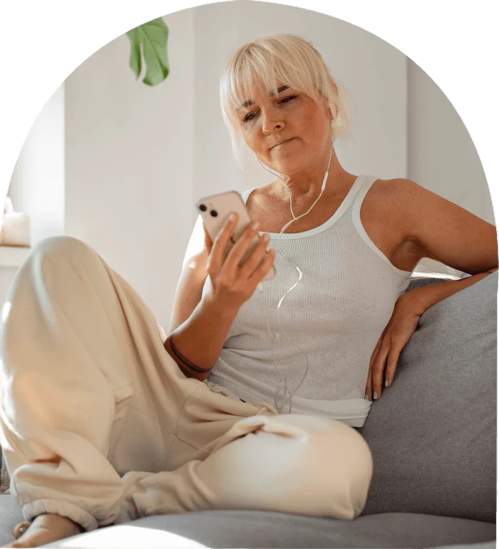 A woman sitting on a couch wearing headphones, looking relaxed and listening to music